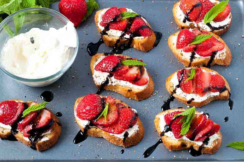 Strawberry Whipped Feta Crostini with Balsamic Drizzle on a baking sheet with a bowl of whipped feta