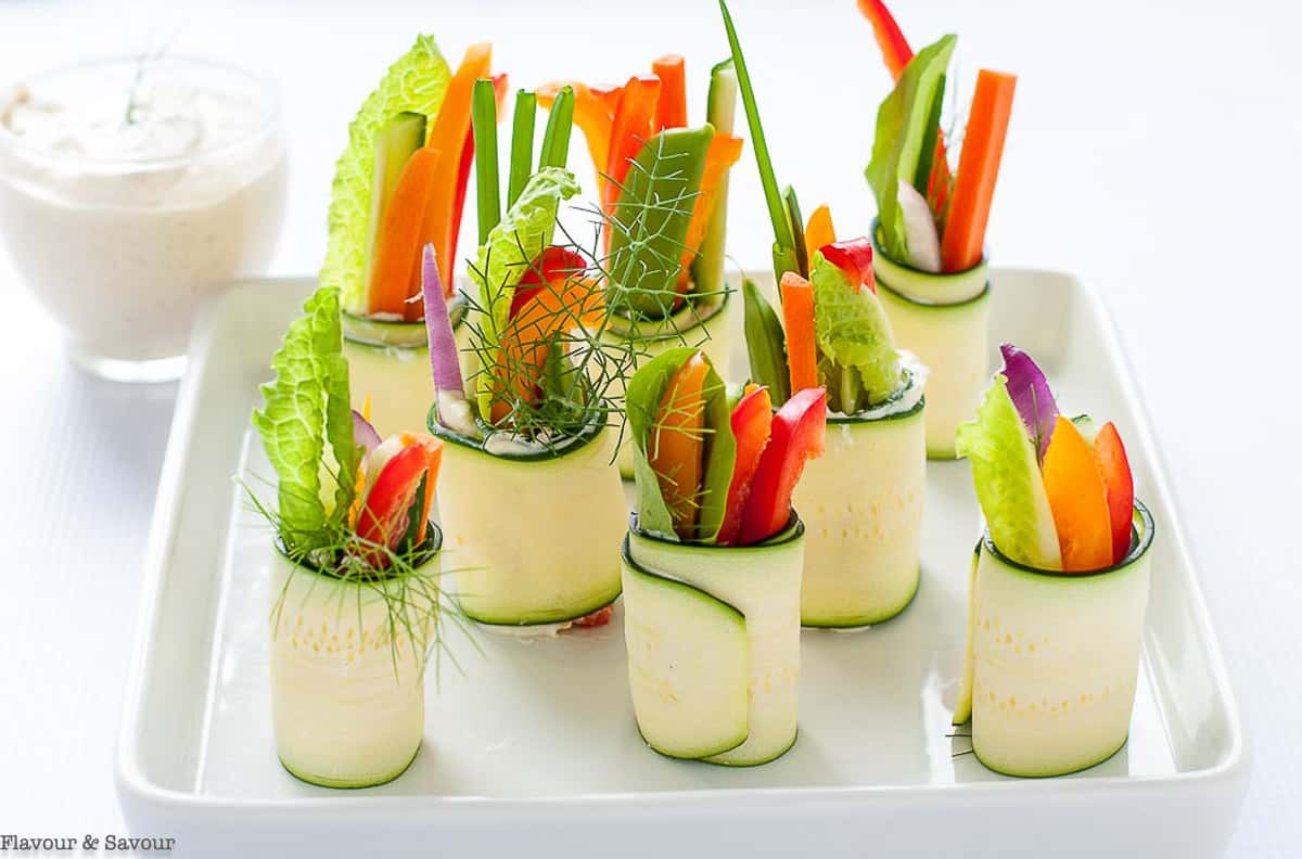 Fresh veggie zucchini roll-up appetizers on a white platter.