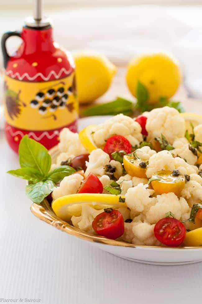  Cauliflower Lemon Basil Salad in a bowl with oil dispenser and fresh lemons in background.