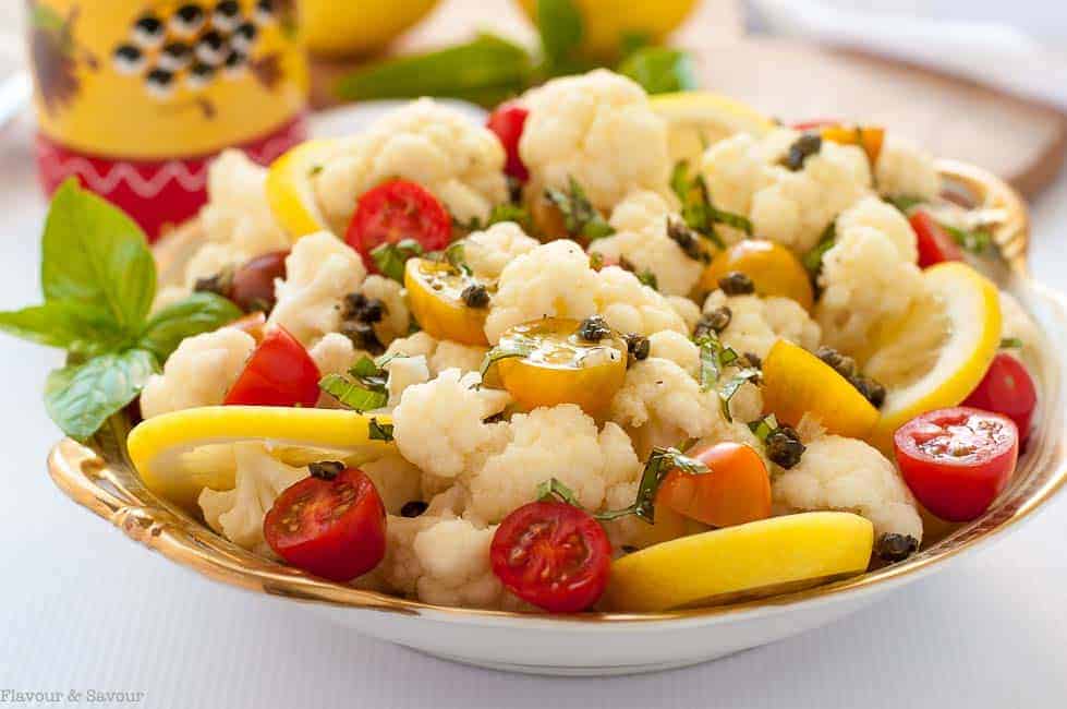 Cauliflower lemon basil salad with toasted capers garnished with tomatoes, lemon slices and fresh basil.