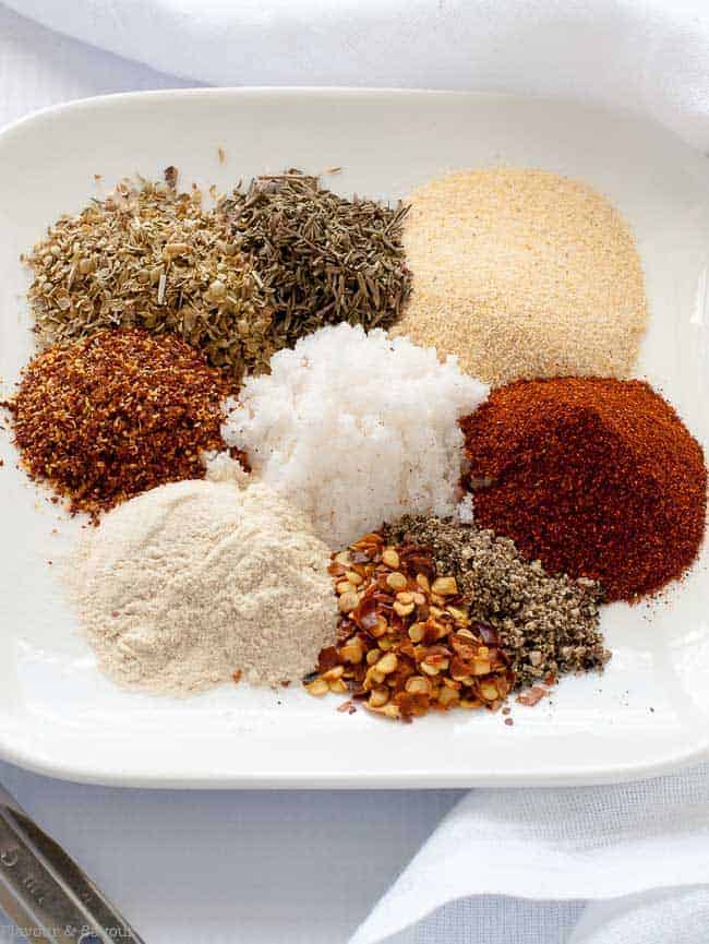 Spices and herbs for Cajun seasoning mix in mounds on a white plate.