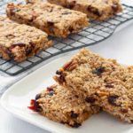 Cranberry Pecan Oat bars on a cooling rack and stacked on a plate.