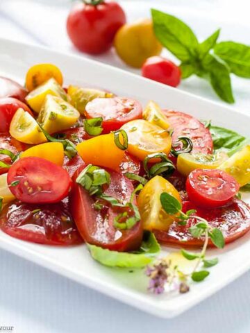 Heirloom tomato salad with basil and feta on a white platter