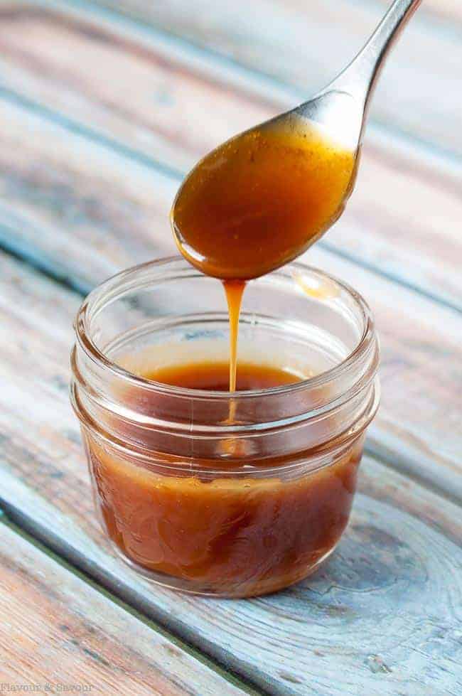 Spooning vegan caramel sauce into a small jar.