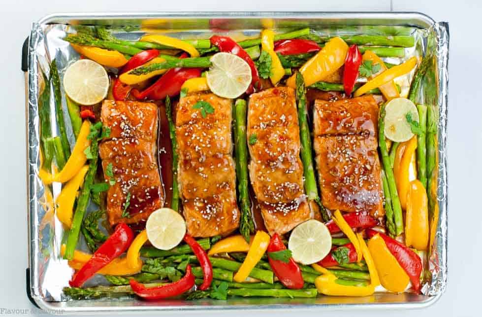 Thai Chili Salmon fillets surrounded by asparagus spears and red and yellow peppers on a sheet pan