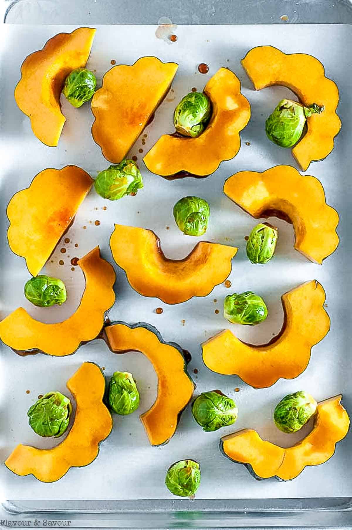 Balsamic acorn squash slices with Brussels sprouts on a baking sheet.
