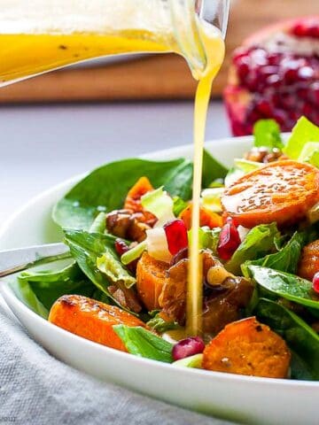 pouring hone-dijon vinaigrette on spinach salad with roasted sweet potatoes