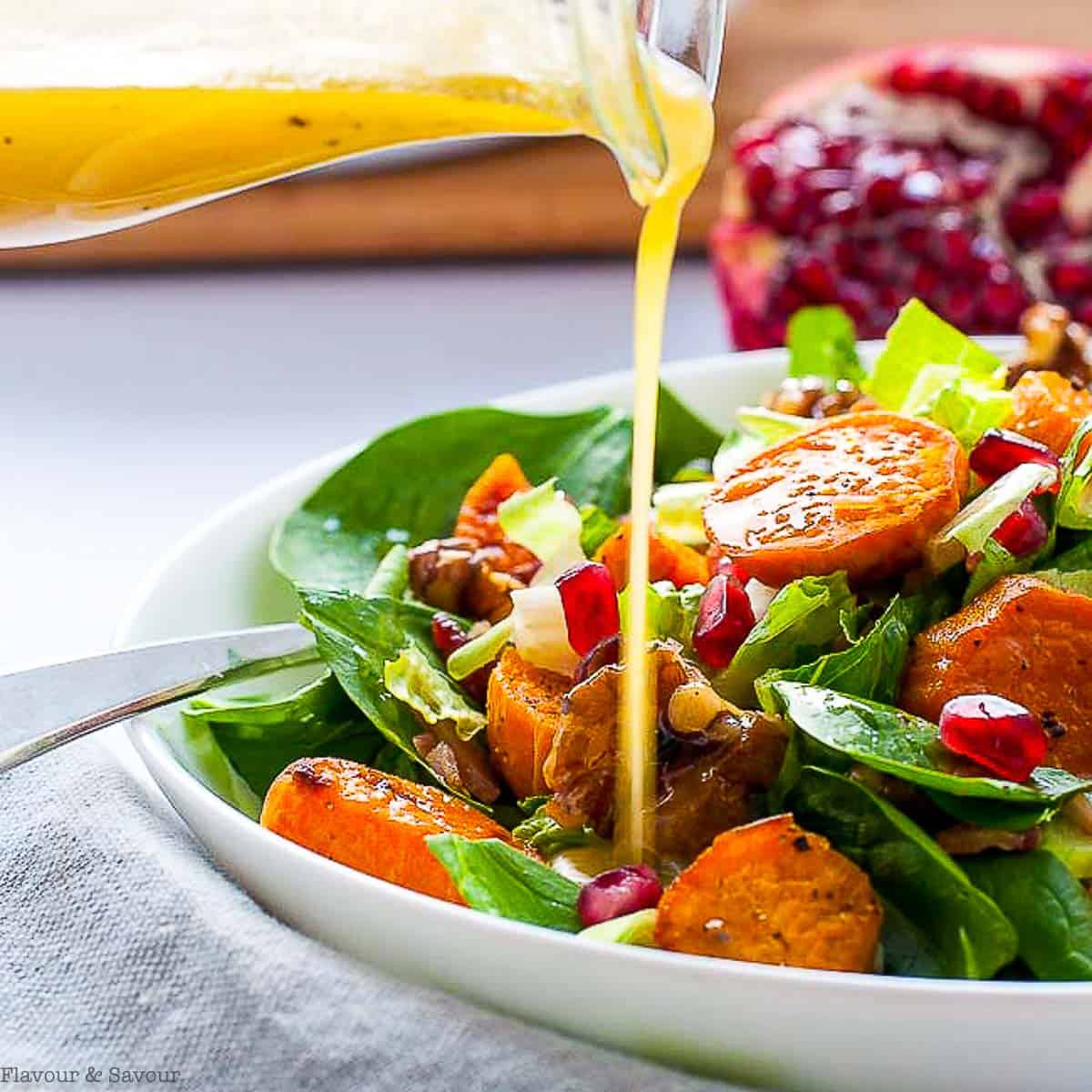 pouring hone-dijon vinaigrette on spinach salad with roasted sweet potatoes