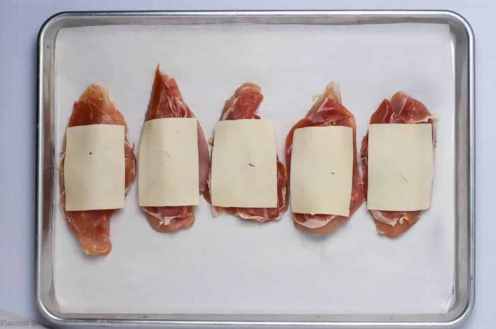 Preparing Chicken for by covering with prosciutto and sliced cheese for Prosciutto and Cheesy Chicken Sheet Pan Dinner