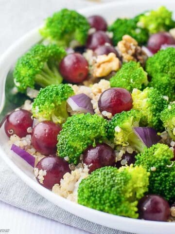 A bowl of broccoli quinoa salad with grapes and walnuts.
