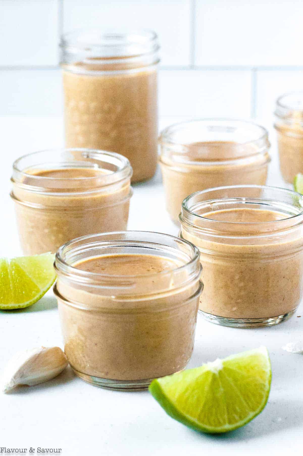Small jars of peanut sauce with lime slices beside them.