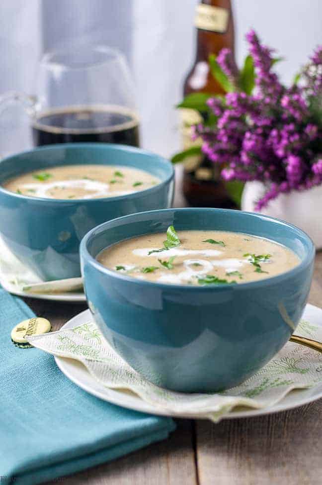 Creamy Roasted Garlic Irish Potato Soup in turquoise bowls with a mug of Guinness