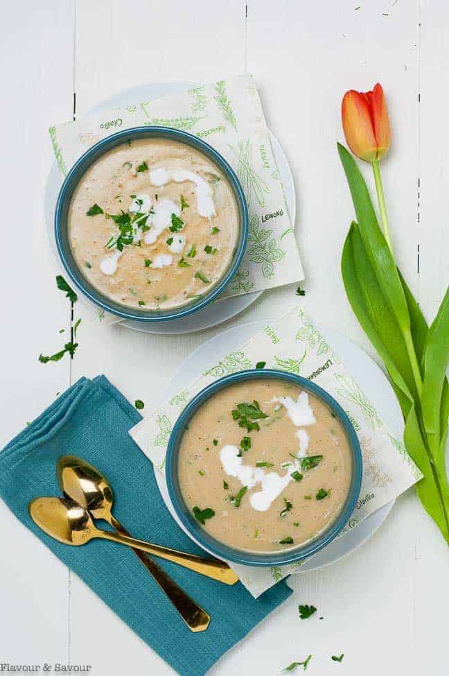 Overhead view of Creamy Roasted Garlic Irish Potato Soup in blue bowls with a tulip beside