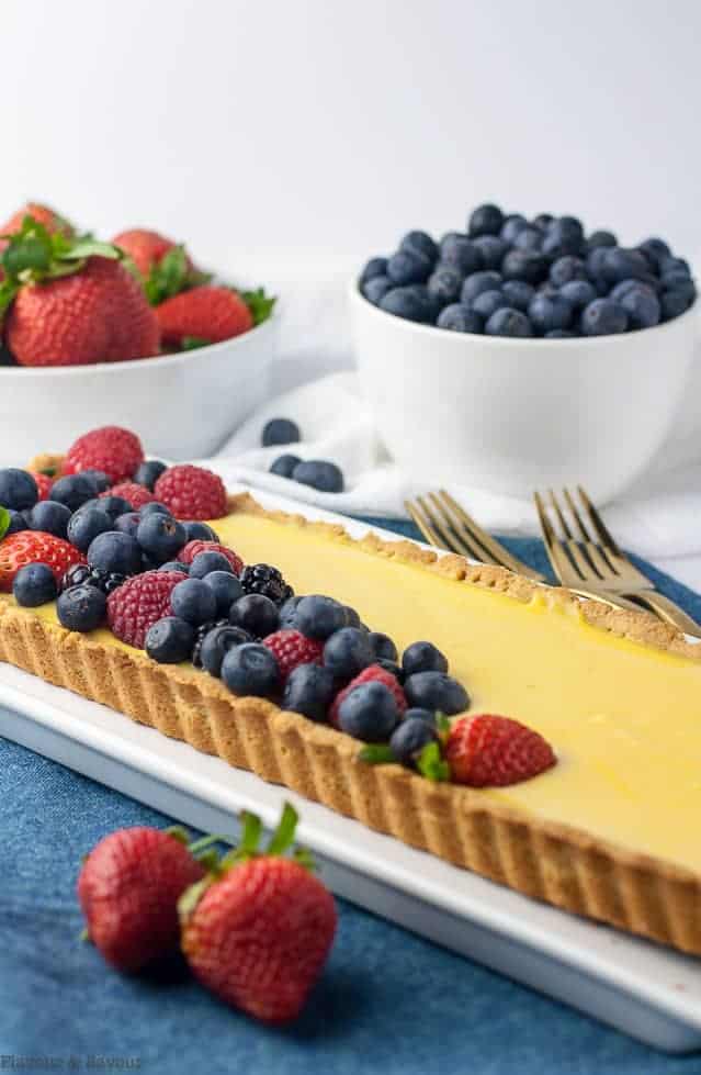 Side view of Gluten-Free Lemon Curd Tart with bowls of berries