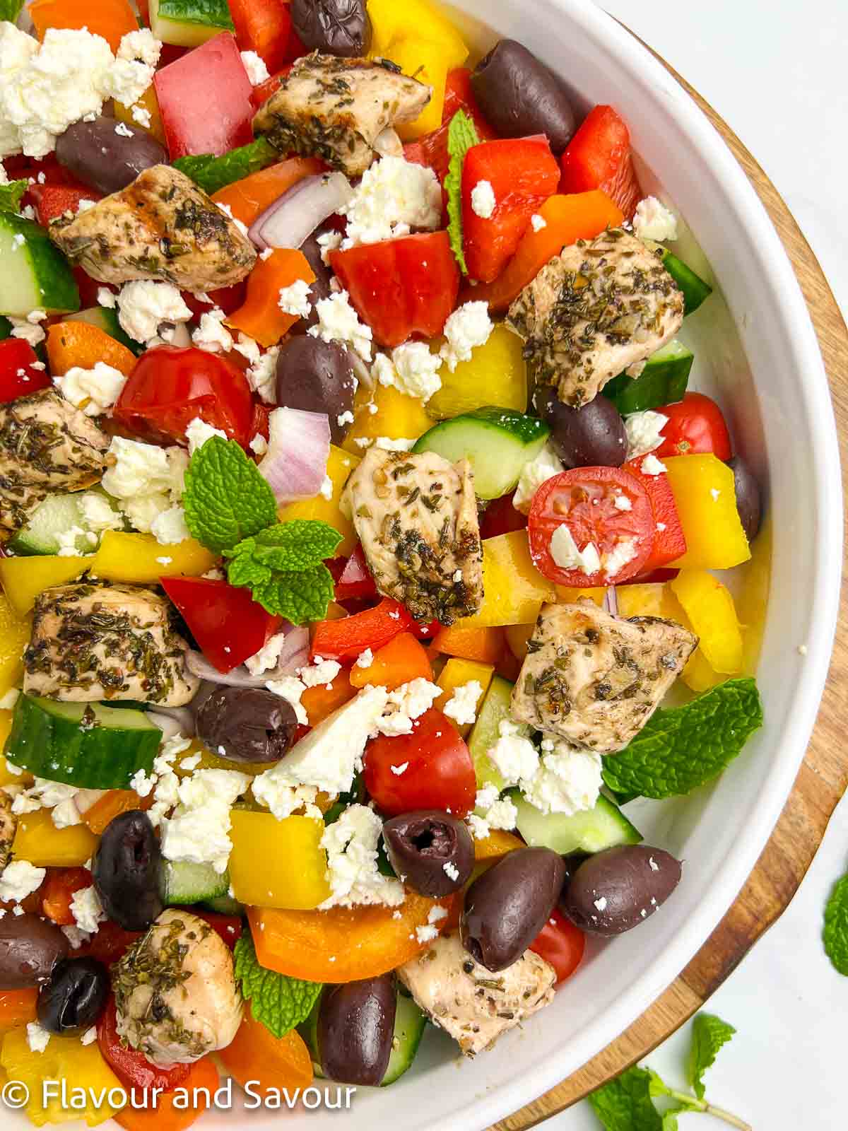 Close-up overhead view of a shallow bowl of Greek Chicken Salad with grilled chicken and colourful vegetables, part of a collection of Greek chicken recipes.