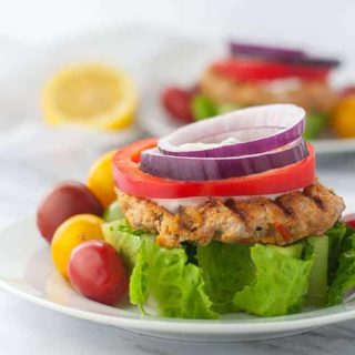 Open Face Harissa Chicken Burger on a wedge of lettuce garnished with red onion and red pepper rings and Greek Yogurt Sauce