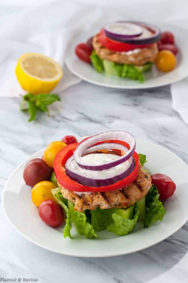 Two Open-Faced Harissa Chicken Burger on a wedge of lettuce garnished with red onion and red pepper rings and Greek Yogurt Sauce