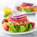 An open-faced harissa flavoured chicken burger with lettuce tomato and red onion.