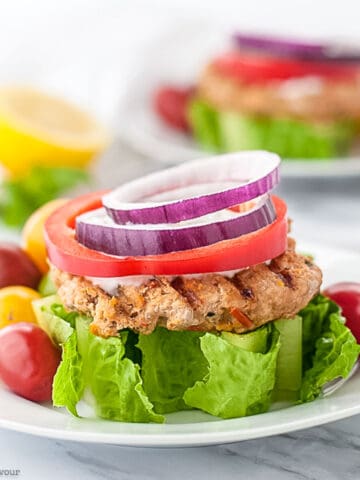 An open-faced harissa flavoured chicken burger with lettuce tomato and red onion.
