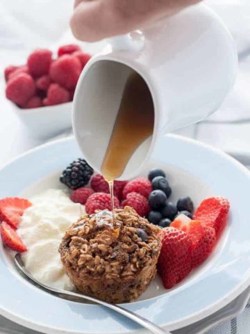 Pouring maple syrup on Mixed Berry Baked Oatmeal Cups with Chia and Kefir.