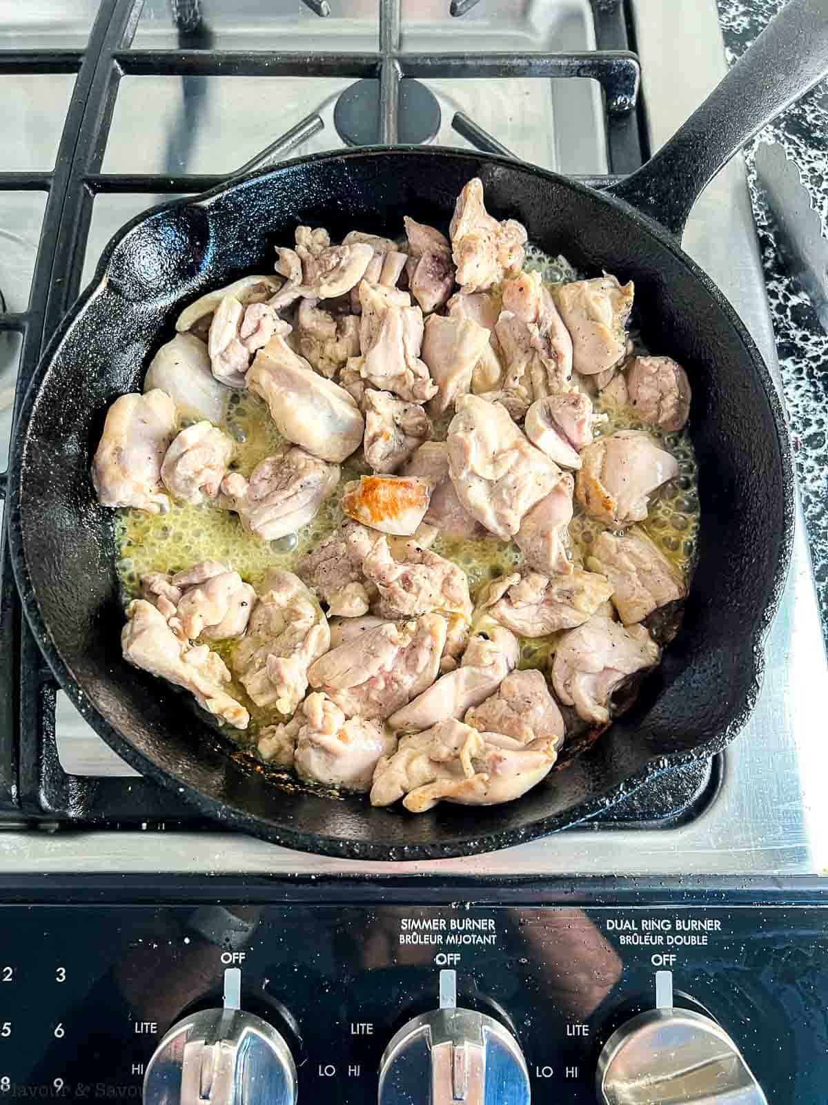 Browning chicken pieces in a cast iron skillet.