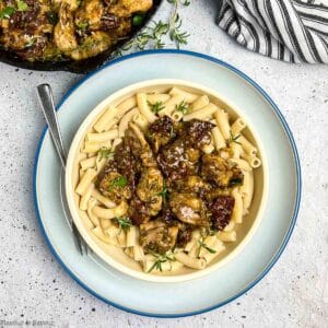 A bowl of pasta topped with sun dried tomato and artichoke chicken.