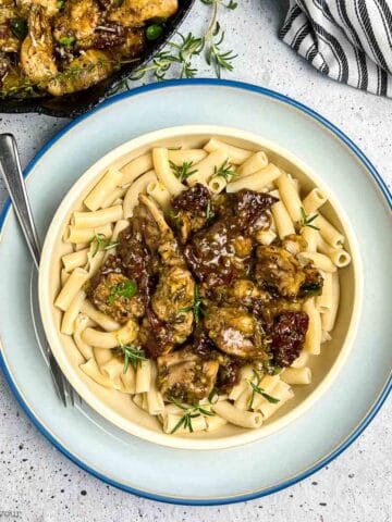 A bowl of pasta topped with sun dried tomato and artichoke chicken.