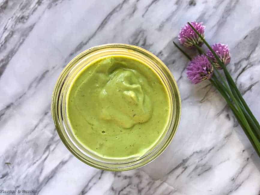 Mayo-Free Avocado Green Goddess Dressing in a jar with chive flowers