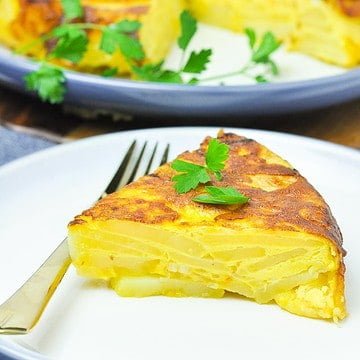 Close up view of a wedge of tortilla española on a plate with a fork.