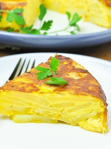 Close up view of a wedge of tortilla española on a plate with a fork.