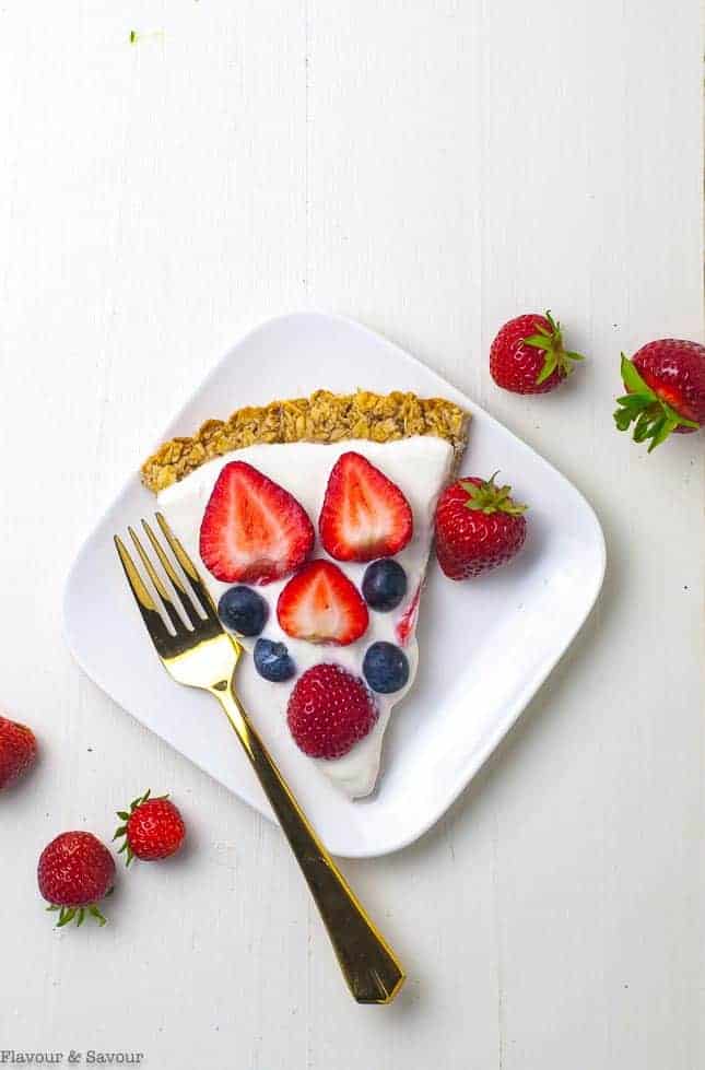 A wedge of Gluten-free Breakfast Fruit Pizza on a plate with fresh strawberries and blueberries