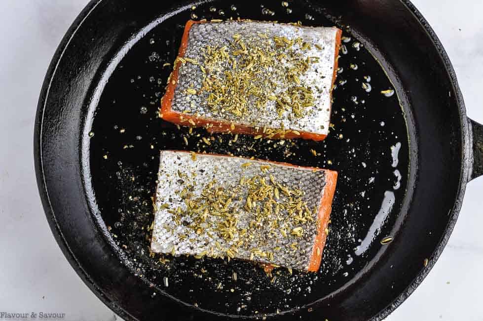 Salmon skin side up in a cast iron pan.