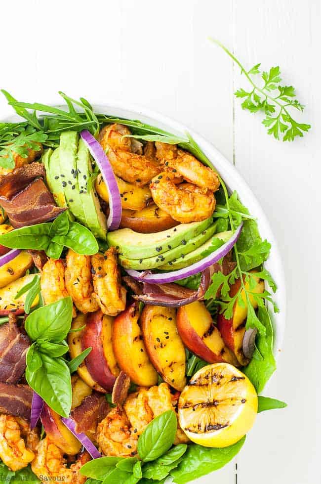 Avocado Grilled Peach and Chipotle Shrimp Salad with Bacon arranged in a round white shallow dish on a white background