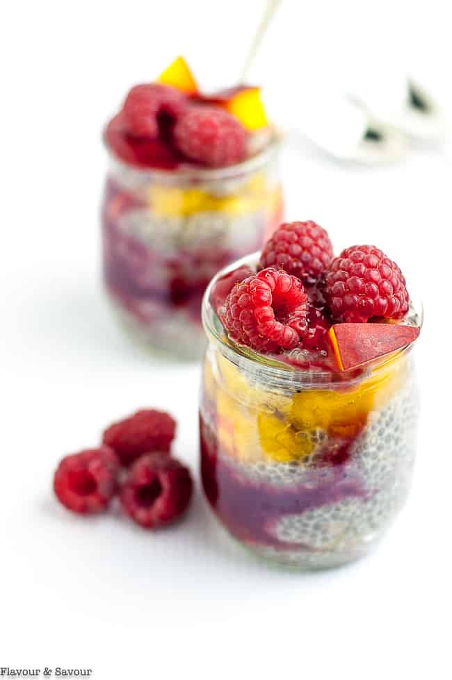 Two mini jars of raspberry peach chia seed pudding with fresh raspberries