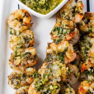 Grilled Chimichurri Shrimp Skewers on a platter with a bowl of Chimichurri Dipping Sauce