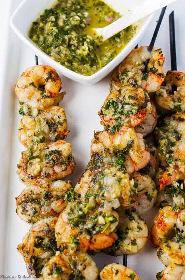 Grilled Chimichurri Shrimp Skewers on a platter with a bowl of Chimichurri Dipping Sauce