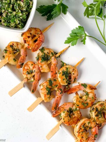 Appetizer size Chimichurri shrimp kabobs on a white platter.