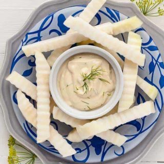 raw kohlrabil sticks on a blue patterned plate with a bowl of Dijon Dilly Dip