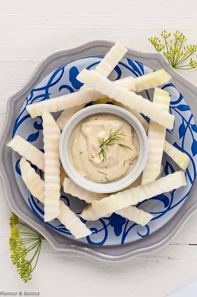 raw kohlrabil sticks on a blue patterned plate with a bowl of Dijon Dilly Dip