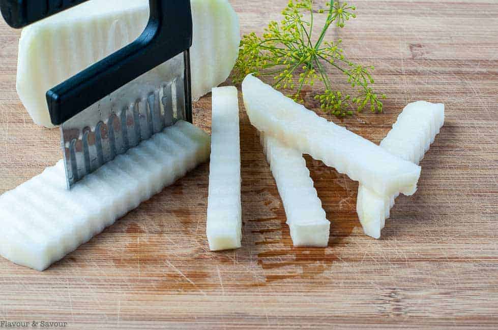 Using a handheld crinkle cutter to cut raw kohlrabi veggie sticks