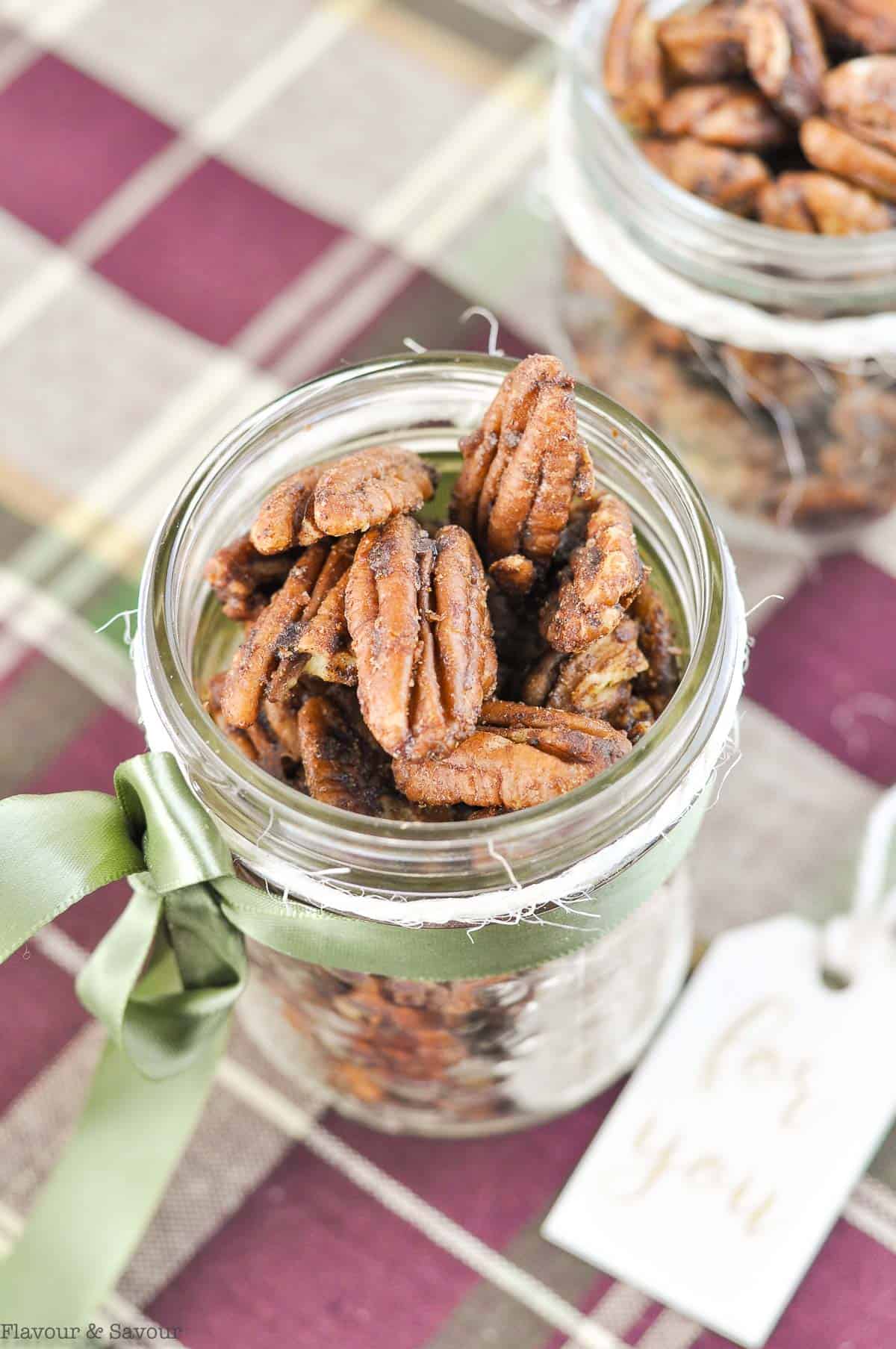 Close up view of spiced pecans in a jar with a ribbon and tag