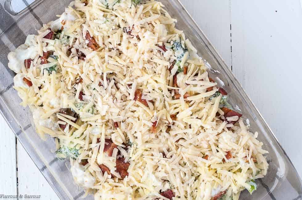 Sprinkling Parmesan on Cheesy Broccoli Cauliflower Casserole with Bacon