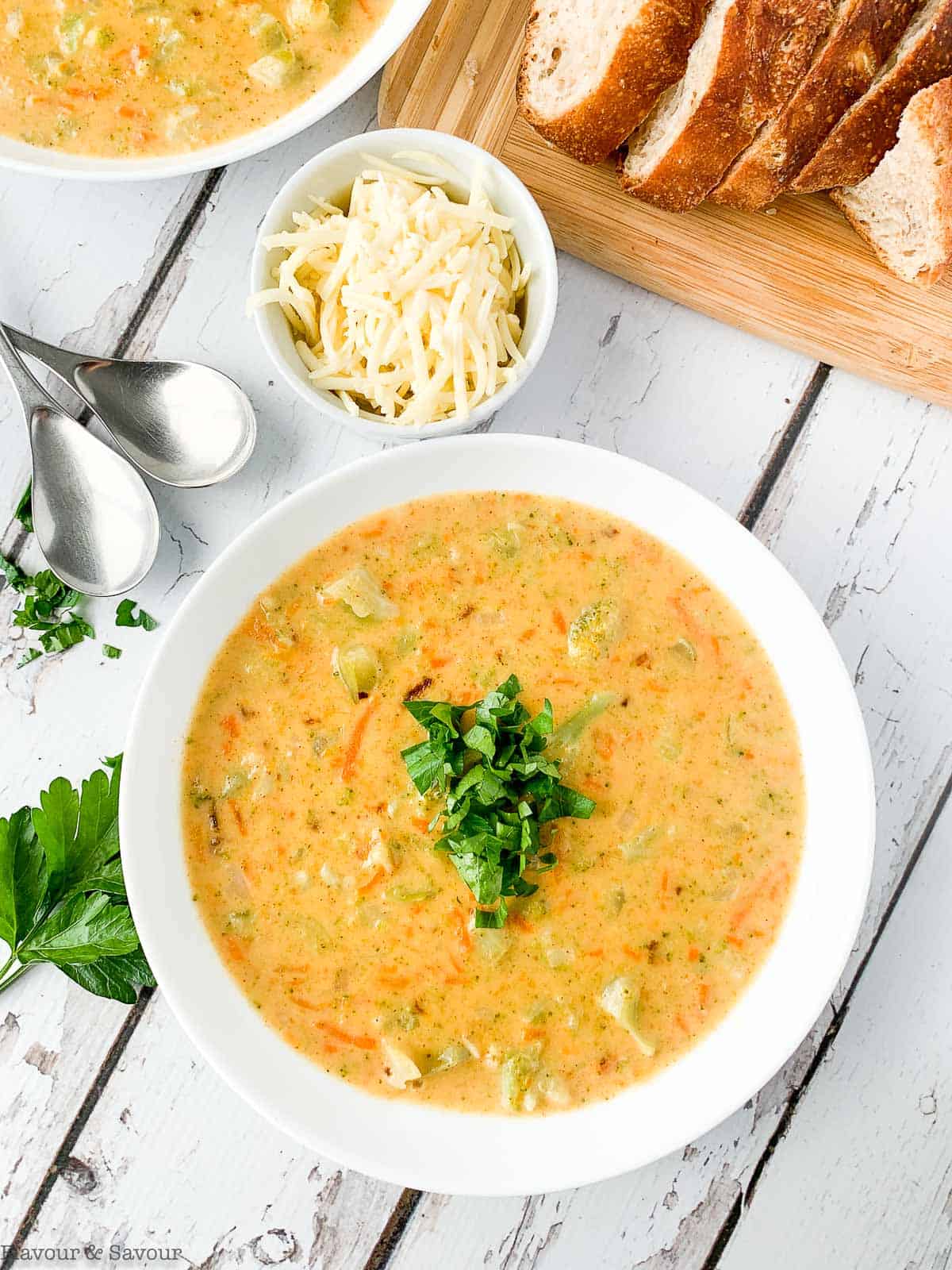 A bowl of Broccoli White Cheddar soup with bread slices and a bowl of grated cheese.