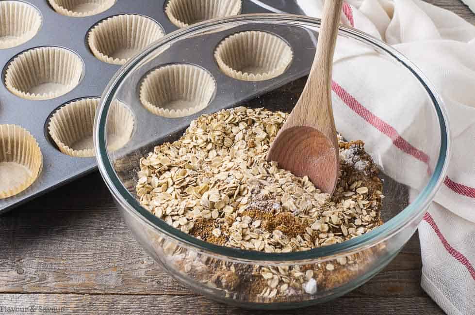 Cranberry-Apple Pumpkin Baked Oatmeal dry ingredients in a glass bowl with a wooden spoon. 