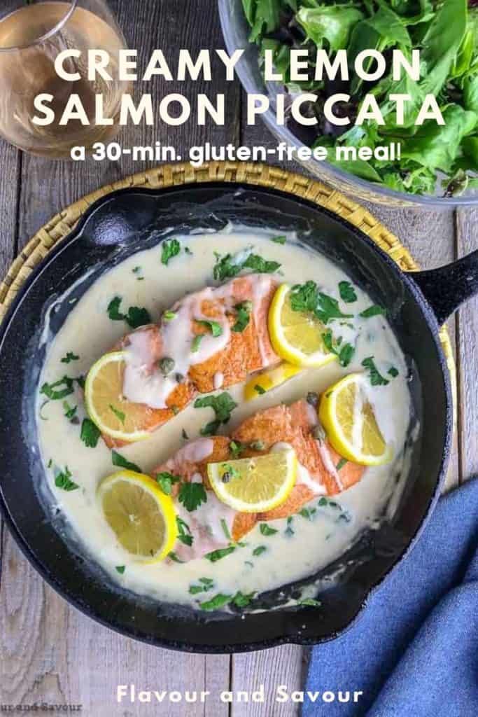 Creamy Lemon Salmon Piccata in a cast iron pan garnished with lemon slices with a salad in the background