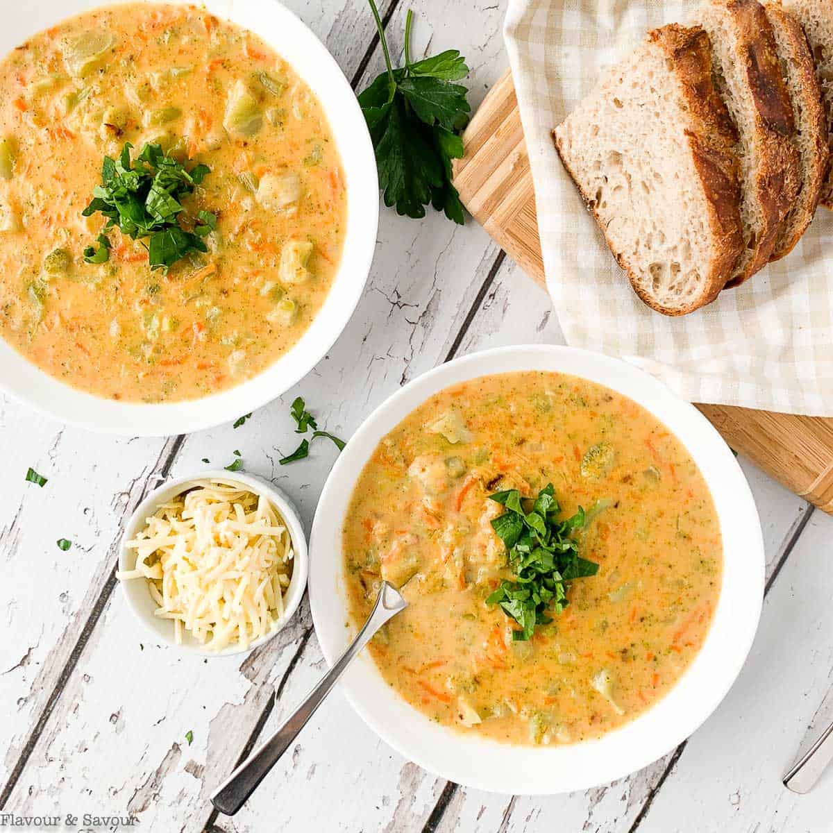 Two bowls of Broccoli White Cheddar with bread slices on a board.