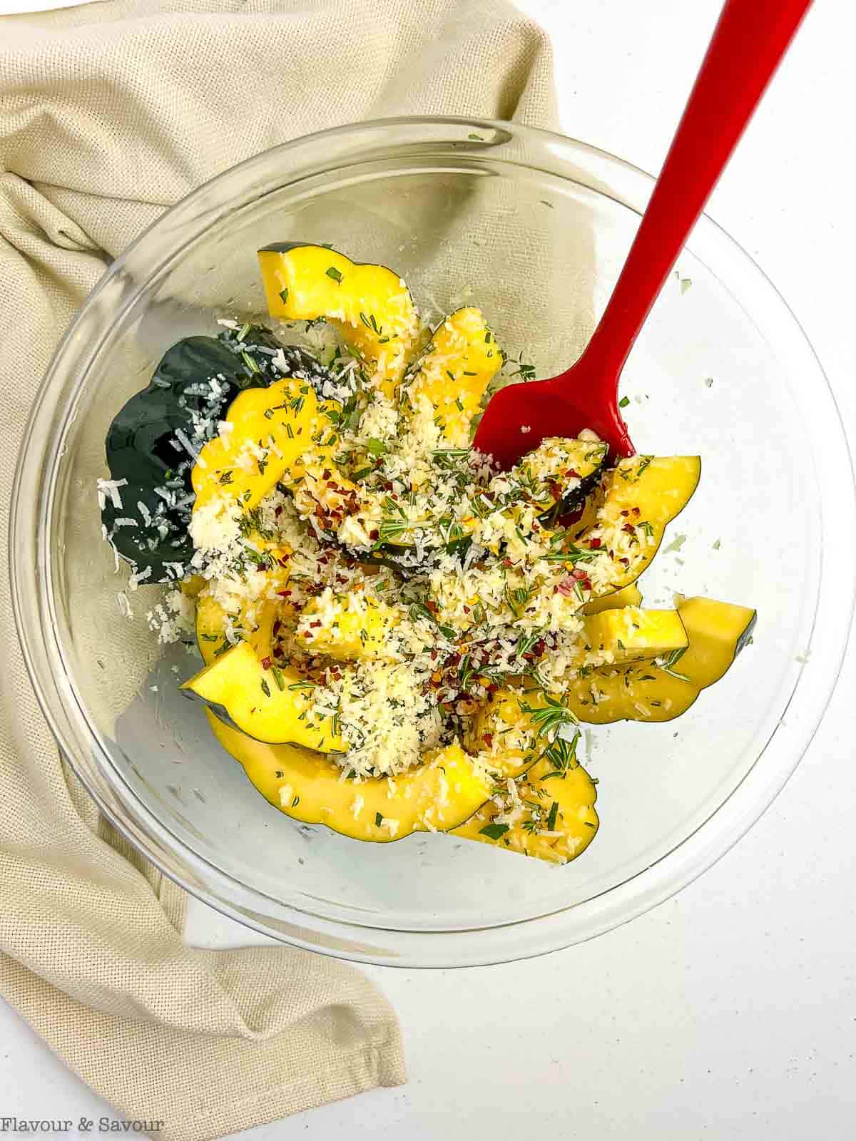 Slices of acorn squash in a bowl with fresh garlic, fresh herbs and parmesan cheese.