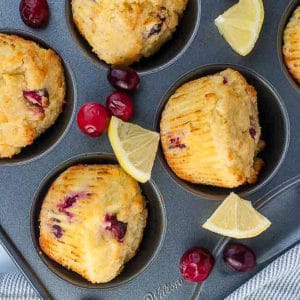 Baked cranberry lemon muffins in a muffin tin with lemon wedges