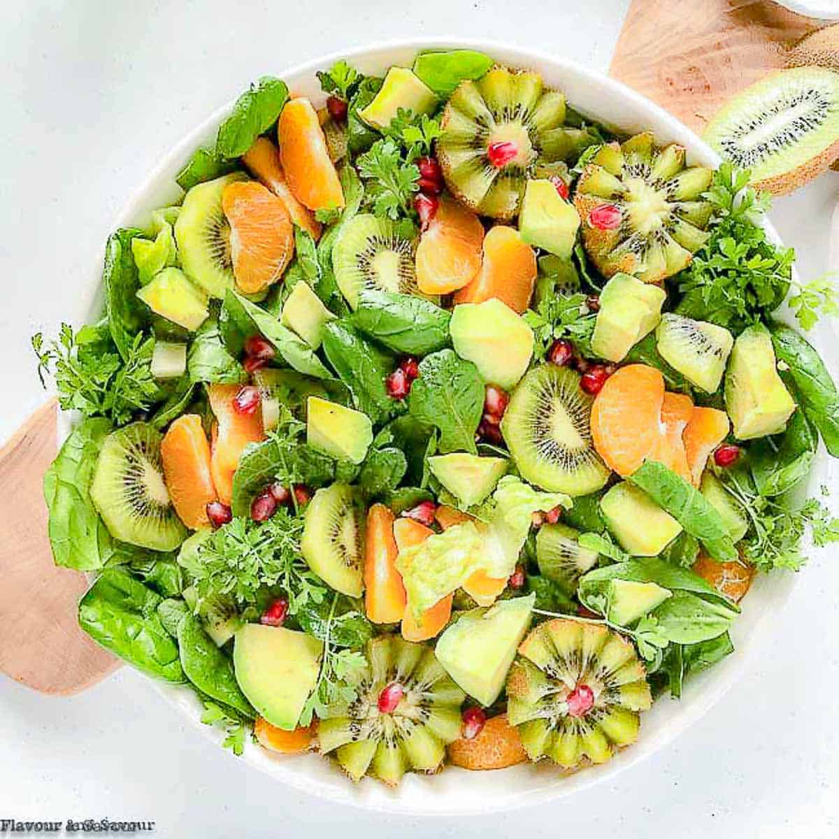 Overhead view of a round white bowl filled with Kiwi Mandarin Spinach Salad with kiwi flowers