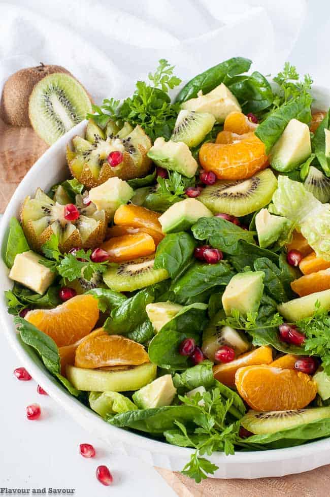 overhead view Kiwi Mandarin Spinach Salad showing baby spinach leaves, orange segments, sliced kiwi, cubed avocado and pomegranate arils.